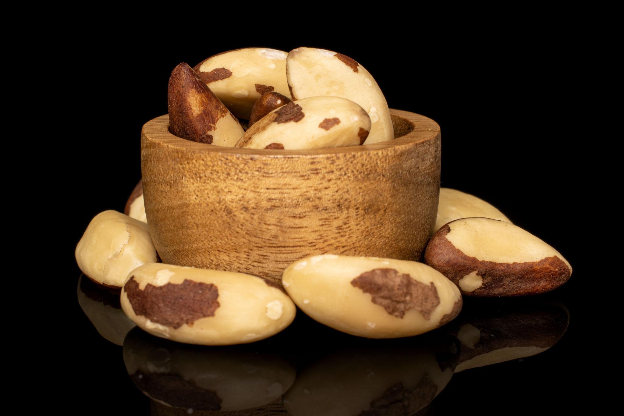 Wooden bowl of shelled Brazil nuts on black glass